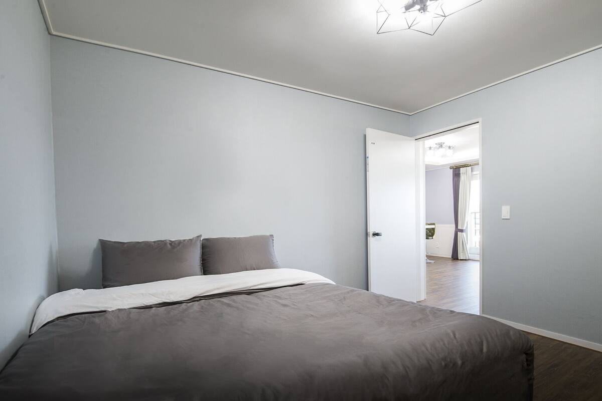 A bedroom with a bed, a door leading to another room, and a ceiling light fixture.
