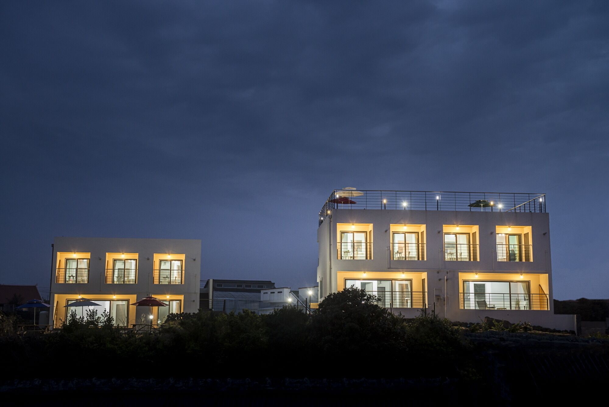 Un bâtiment moderne à deux étages, doté de nombreuses fenêtres illuminées et d’un balcon.