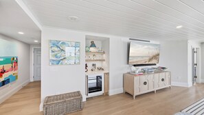 A modern interior with a wooden floor, a white wall with a painting, a built-in shelf with decorative items, and a television mounted above a cabinet.