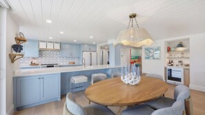 A modern kitchen with light blue cabinets, a central island, and a round wooden dining table with upholstered chairs.