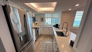 Una cocina moderna con electrodomésticos de acero inoxidable, armarios blancos y un amplio ventanal con vistas a la ciudad.
