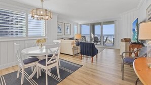 Amplia sala de estar con mesa de comedor, sillas y vista al océano a través de amplias ventanas.