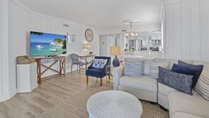 Una sala de estar con televisor, sofá, mesa de centro y comedor con sillas y una lámpara.