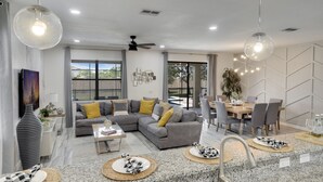 A modern living room with a sectional sofa, dining area, granite countertops, and a large window. - Family Getaway near Disney, Private Pool, Theater, Game Room & Themed Bedrooms (Davenport)