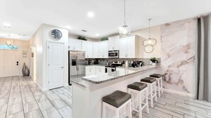 A modern kitchen with white cabinets, a granite countertop, and a marble backsplash. - Family Getaway near Disney, Private Pool, Theater, Game Room & Themed Bedrooms (Davenport)