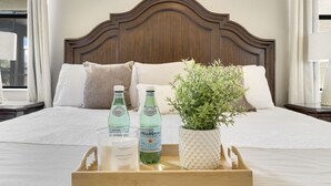 A neatly made bed with a wooden headboard, a tray with two bottles of Pellegrino water, a candle, and a potted plant. - Family Getaway near Disney, Private Pool, Theater, Game Room & Themed Bedrooms (Davenport)
