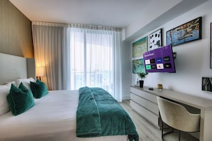 Une chambre d’hôtel avec un lit, un bureau, une télévision et une fenêtre avec des rideaux.