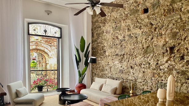 A cozy living room with a stone wall, a sofa, a coffee table, and a dining table with chairs. - Iconic double apartment with billar in front of the Arco Chato ruins  and pool (Ciudad de Panamá)