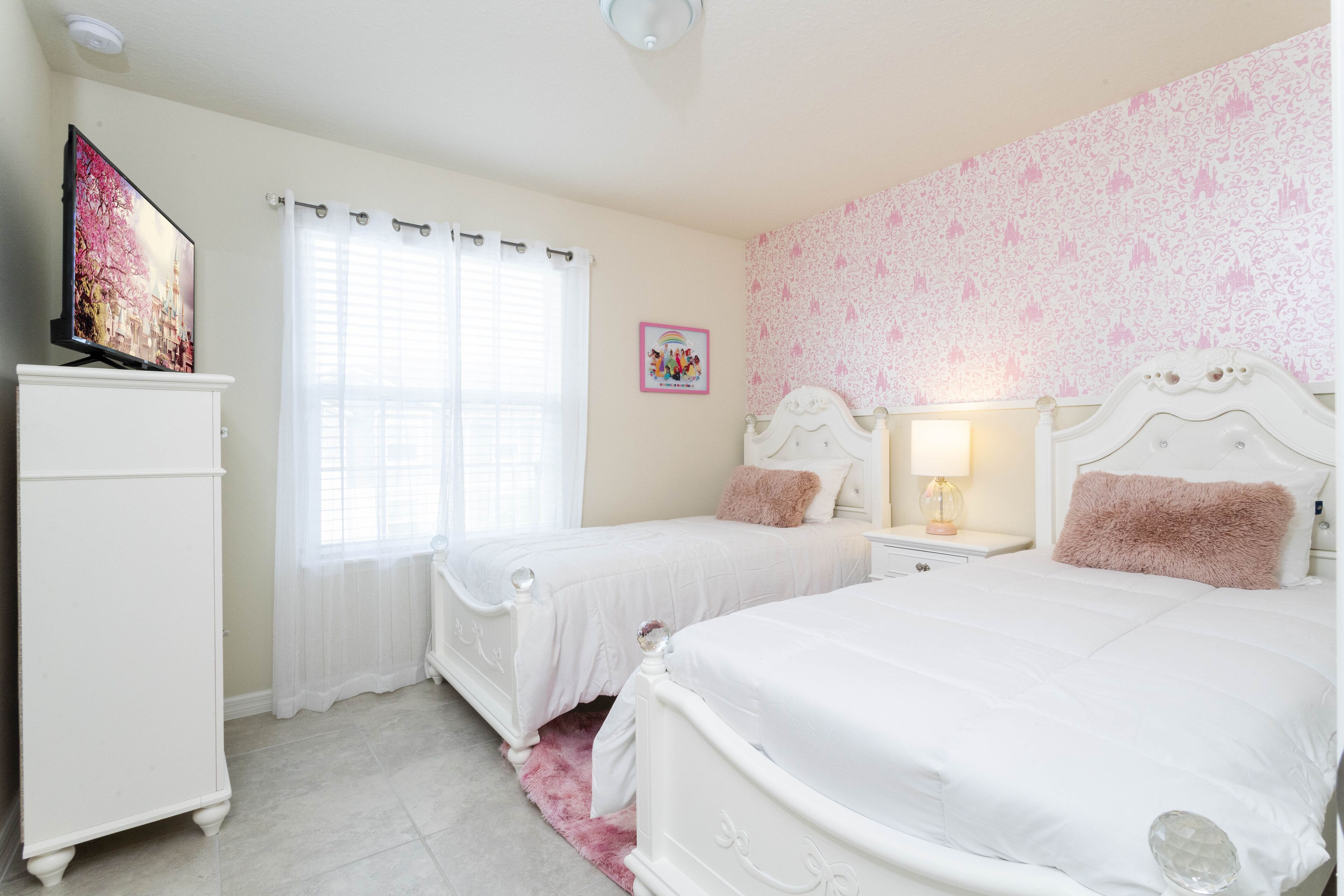 A bedroom with two beds, a TV, a nightstand with a lamp, and a picture on the wall.