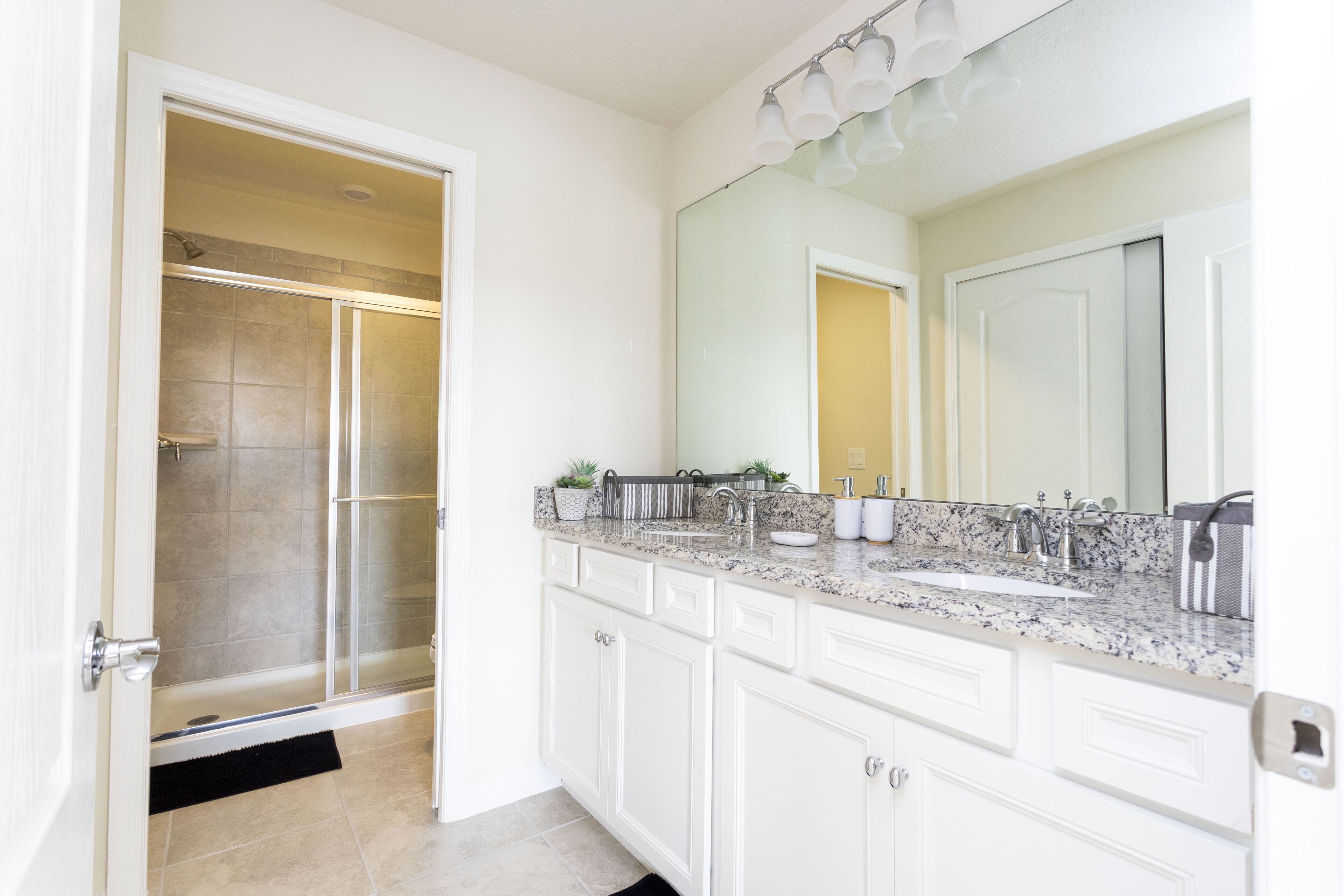 A bathroom with a walk-in shower, a large mirror, and a granite countertop.