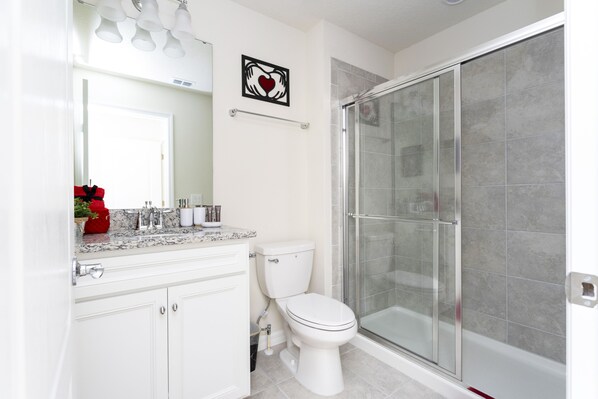 A bathroom with a white toilet, a glass-enclosed shower, and a marble countertop.