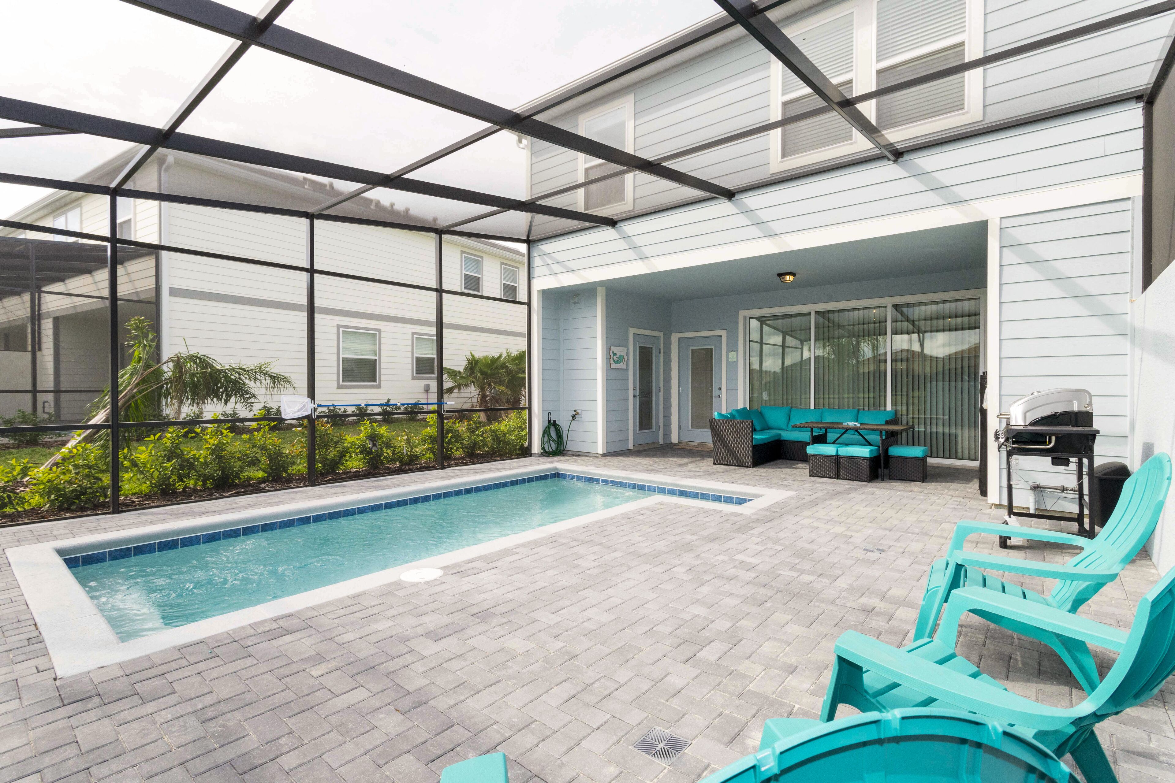 A covered outdoor swimming pool with a patio area, including seating and a grill.