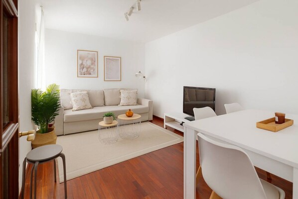 A modern living room with a sofa, coffee table, TV, and dining area.