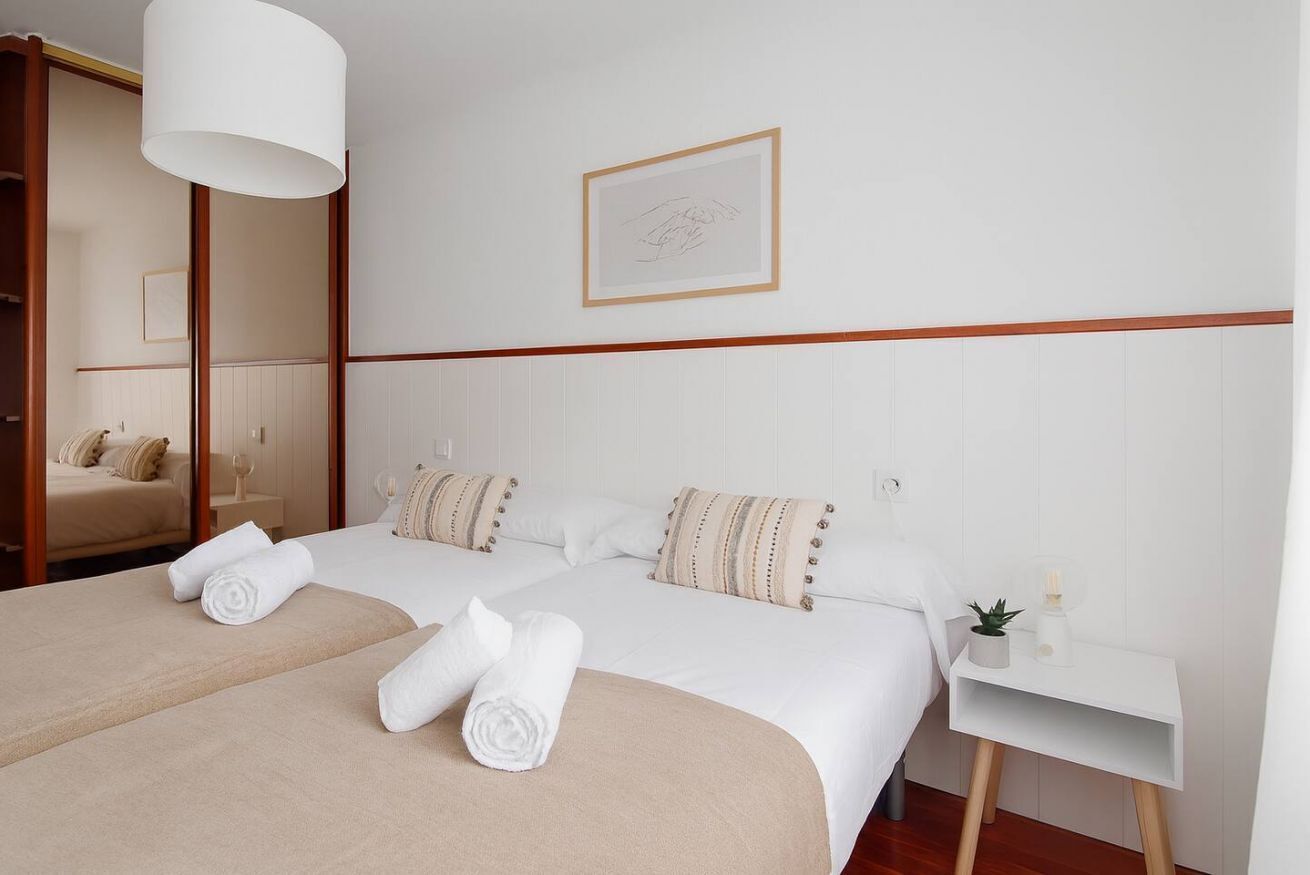 Habitación de hotel con dos camas, una mesita de noche, un espejo y un cuadro en la pared.
