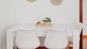 A white dining table with two chairs, a small plant, and two woven wall hangings.
