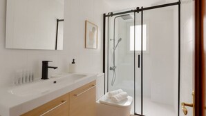 Casa de banho moderna com lavatório branco, espelho e cabine de duche em vidro.