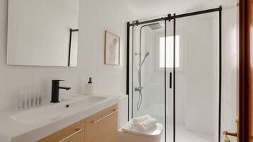 Un baño moderno con un lavamanos blanco, espejo y cabina de ducha de vidrio.