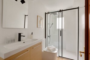 A modern bathroom with a white sink, mirror, and glass shower enclosure.