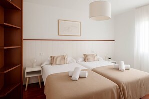 A hotel room with two beds, a nightstand, a lamp, and a framed picture on the wall. - 165A By R2R - 2-Bedroom Apartment (Gijón)