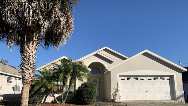 A residential house with a garage, palm trees, and a well-maintained lawn.
