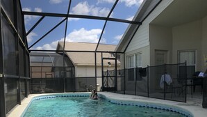 A swimming pool with a glass enclosure, a covered patio, and a view of a house in the background.