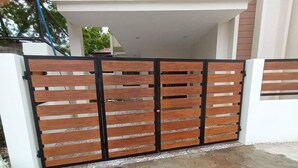 A gated entrance with a wooden and metal gate, a concrete driveway, and a white building in the background. - Elegant/ Centrally located townhouse. (Lapu-Lapu City)