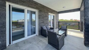 A balcony with a modern design, featuring a glass door, wicker furniture, and a view of the surrounding area.