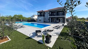 A two-story house with a swimming pool, outdoor seating, and a well-maintained lawn.