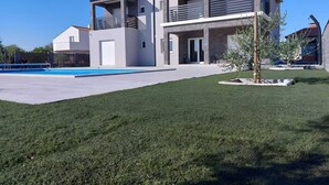 A modern two-story house with a swimming pool, a well-maintained lawn, and a small tree in the front yard.