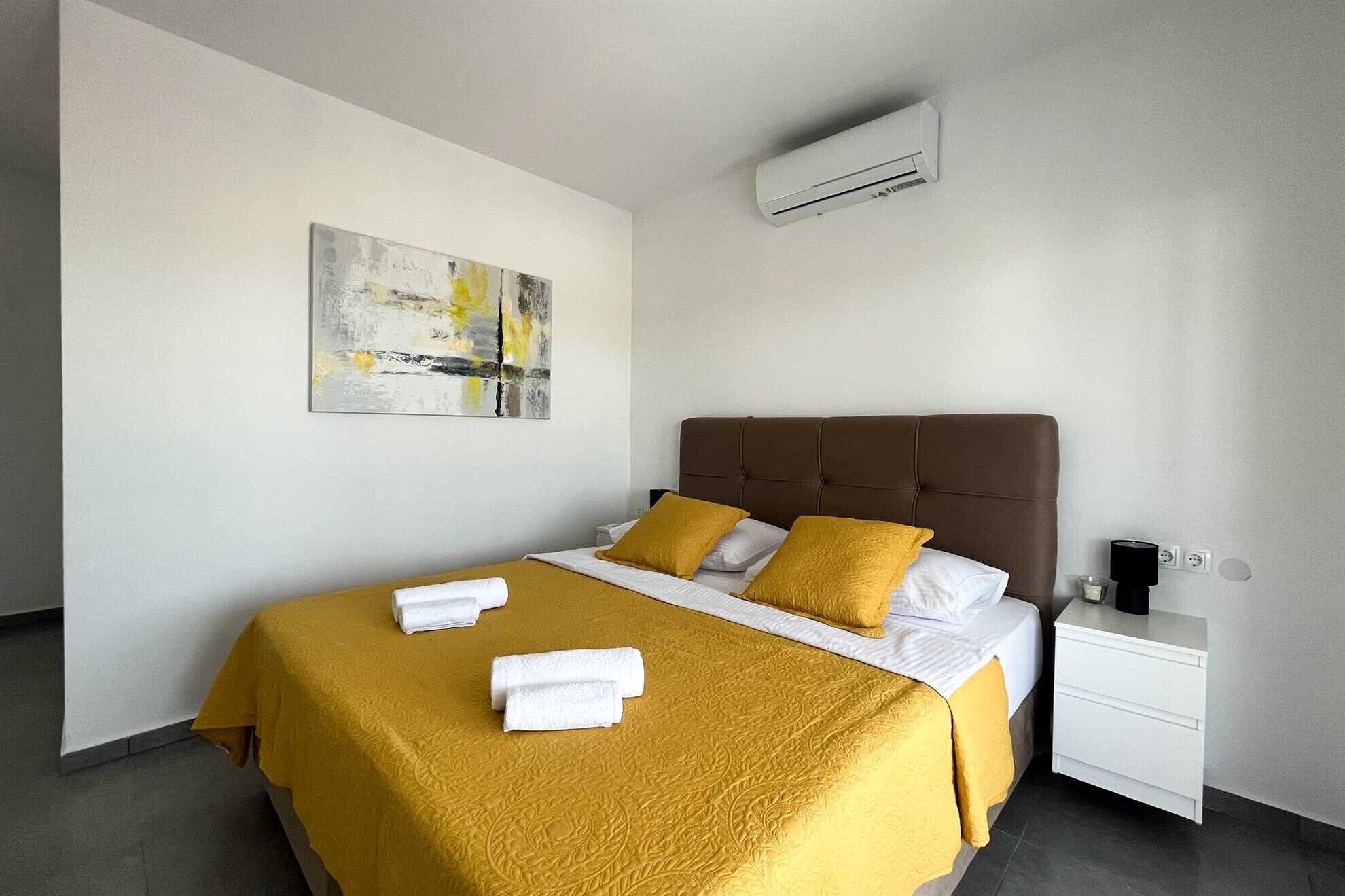 Una camera d'albergo con un letto, un comodino, un condizionatore d'aria e un quadro appeso al muro.