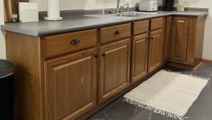 Een keuken met houten kastjes, een granieten aanrechtblad en een inbouwgootsteen. Boven het aanrecht staan planken met servies en glazen.
