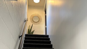 Een trap met een leuning, een potplant en een wandlamp.