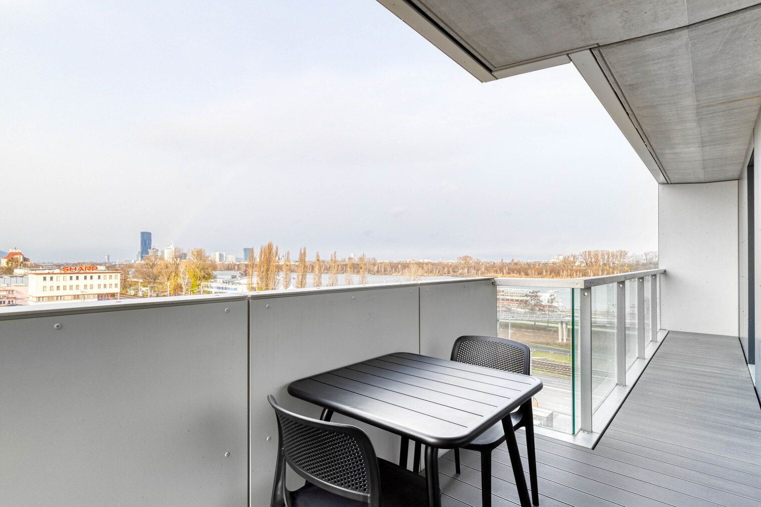 Een balkon met een tafel en stoelen, met uitzicht op een stadsgezicht met gebouwen en bomen.