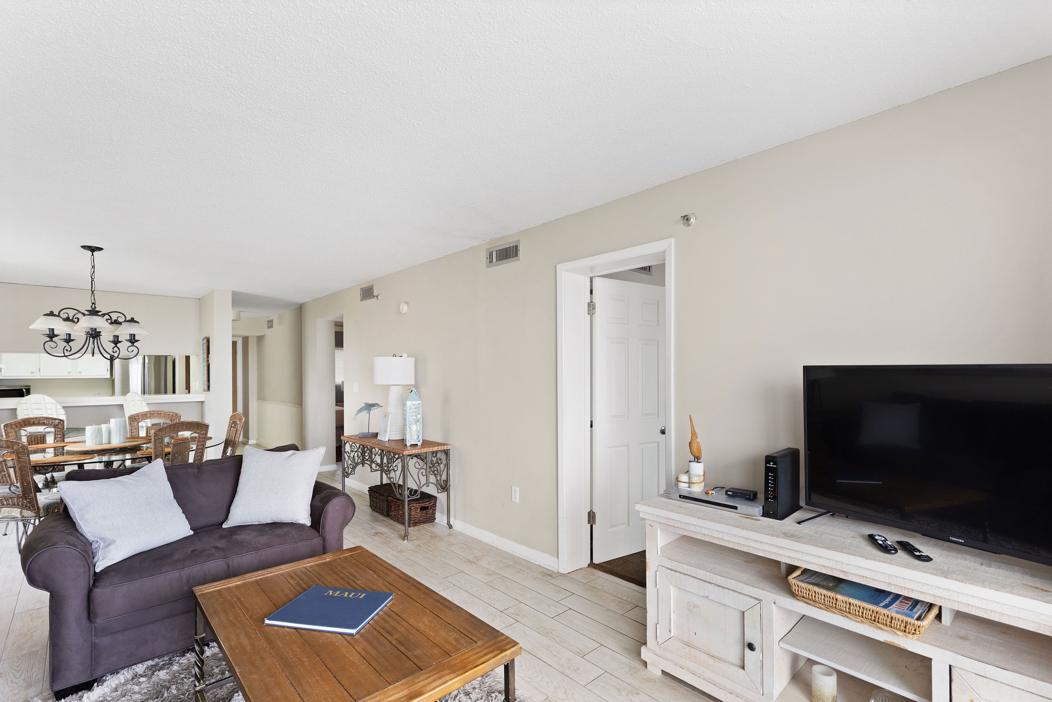A living room with a sofa, coffee table, TV, and a dining area with chairs and a table.