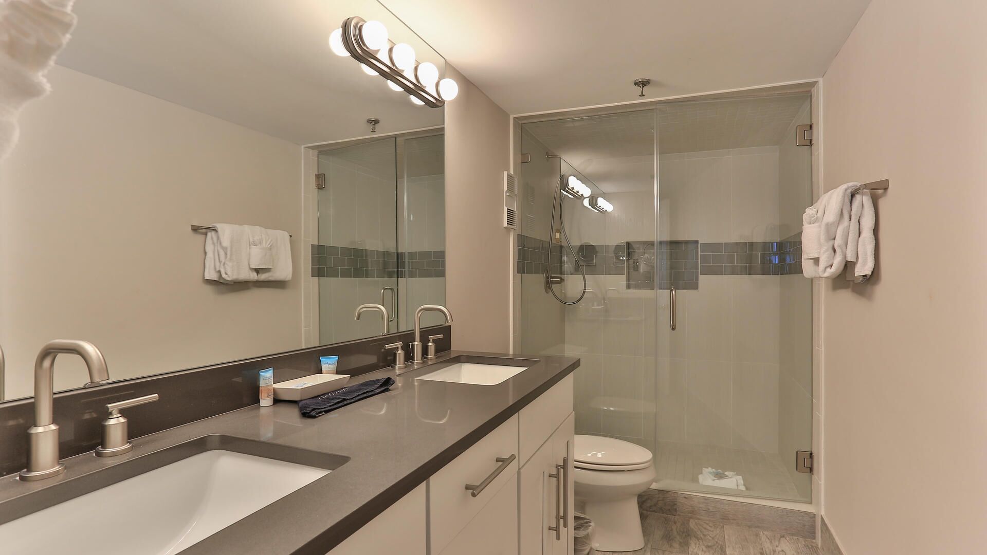 A modern bathroom with a double sink, a glass shower enclosure, and a toilet.