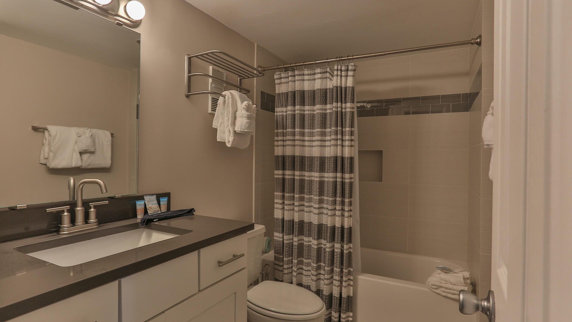 A modern bathroom with a sink, mirror, towel rack, shower curtain, and toilet.