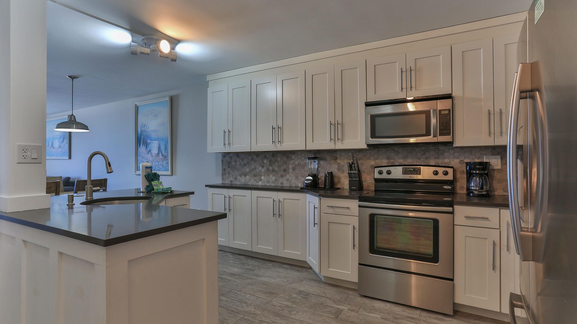 A modern kitchen with white cabinets, stainless steel appliances, a central island, and a pendant light.