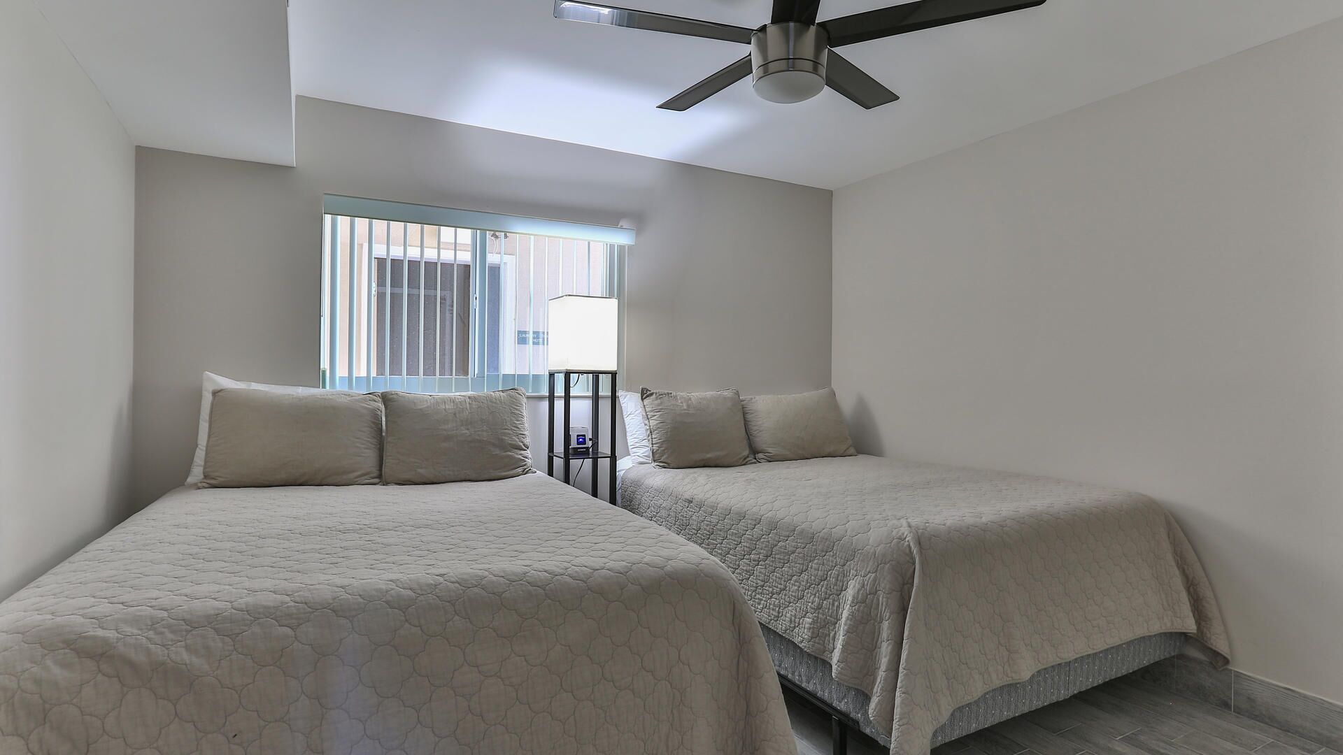 A room with two beds, a ceiling fan, and a window with blinds.