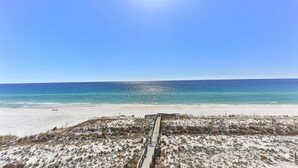 A beach with a wooden boardwalk leading to the water, sandy dunes, and a clear blue sky. - Destin on the Gulf 606 (Destin)