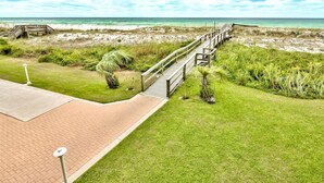 En kyststi der fører til en strand med en træpromenade, grønne områder og frit udsyn over havet.