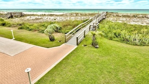 A coastal walkway leading to a beach with a wooden boardwalk, grassy areas, and a clear view of the ocean. - Destin on the Gulf 706- Stunning Gulf Views-Pool (Destin)