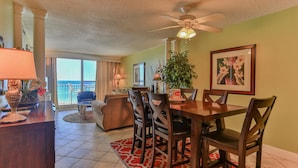 A dining area with a table, chairs, and a view of the ocean through large windows. - Destin on the Gulf 706- Stunning Gulf Views-Pool (Destin)