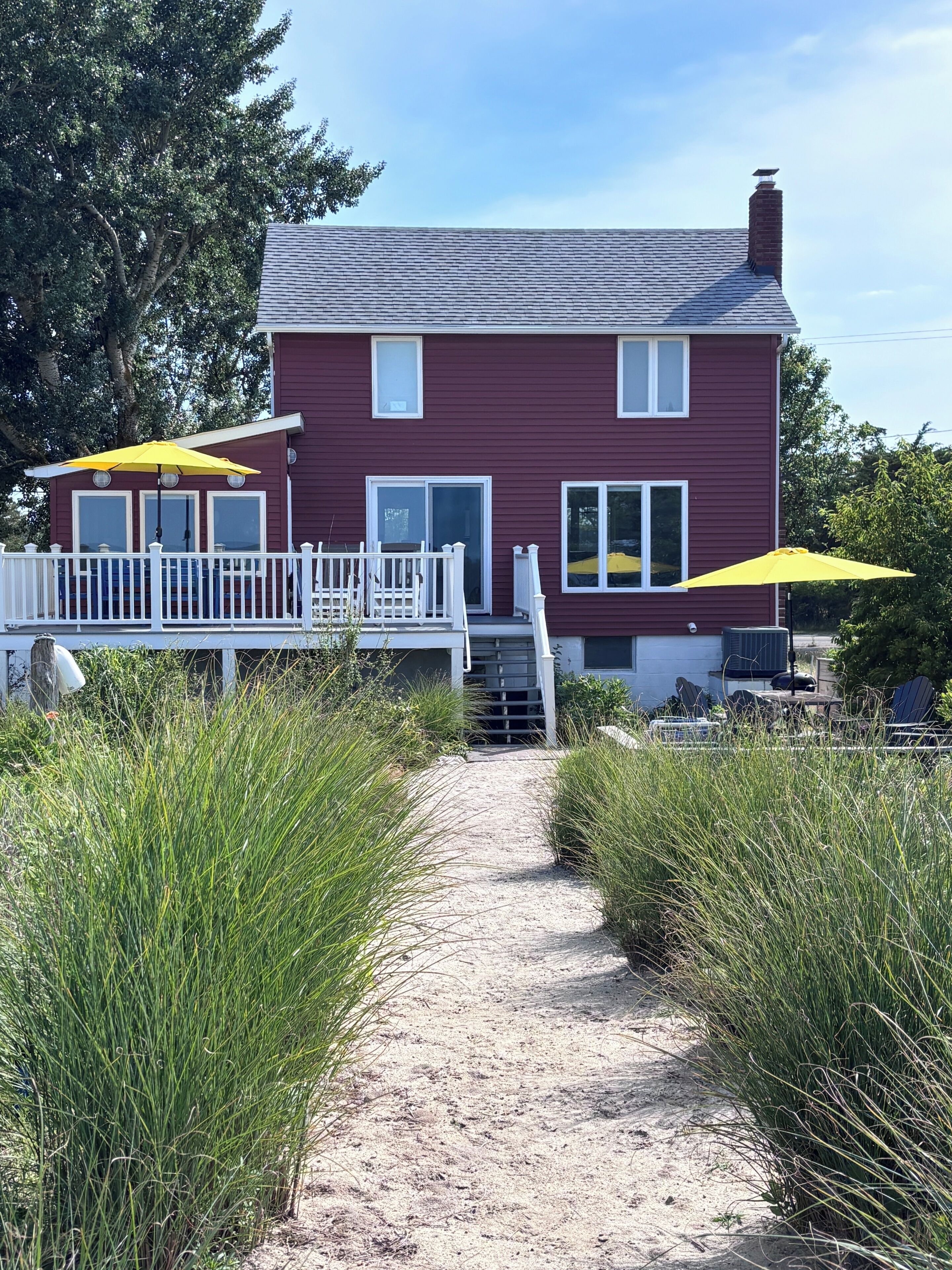A red house with a white porch, a gravel path leading to the entrance, and two yellow umbrellas.