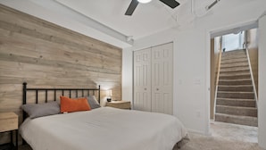 Un dormitorio con cabecera de madera, una cama con edredón blanco, una mesita de noche con lámpara y un armario con puertas blancas.