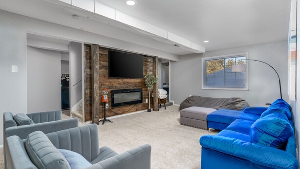 Una sala de estar moderna con chimenea, sofás grises y azules, un televisor de pantalla plana y un ventanal grande.