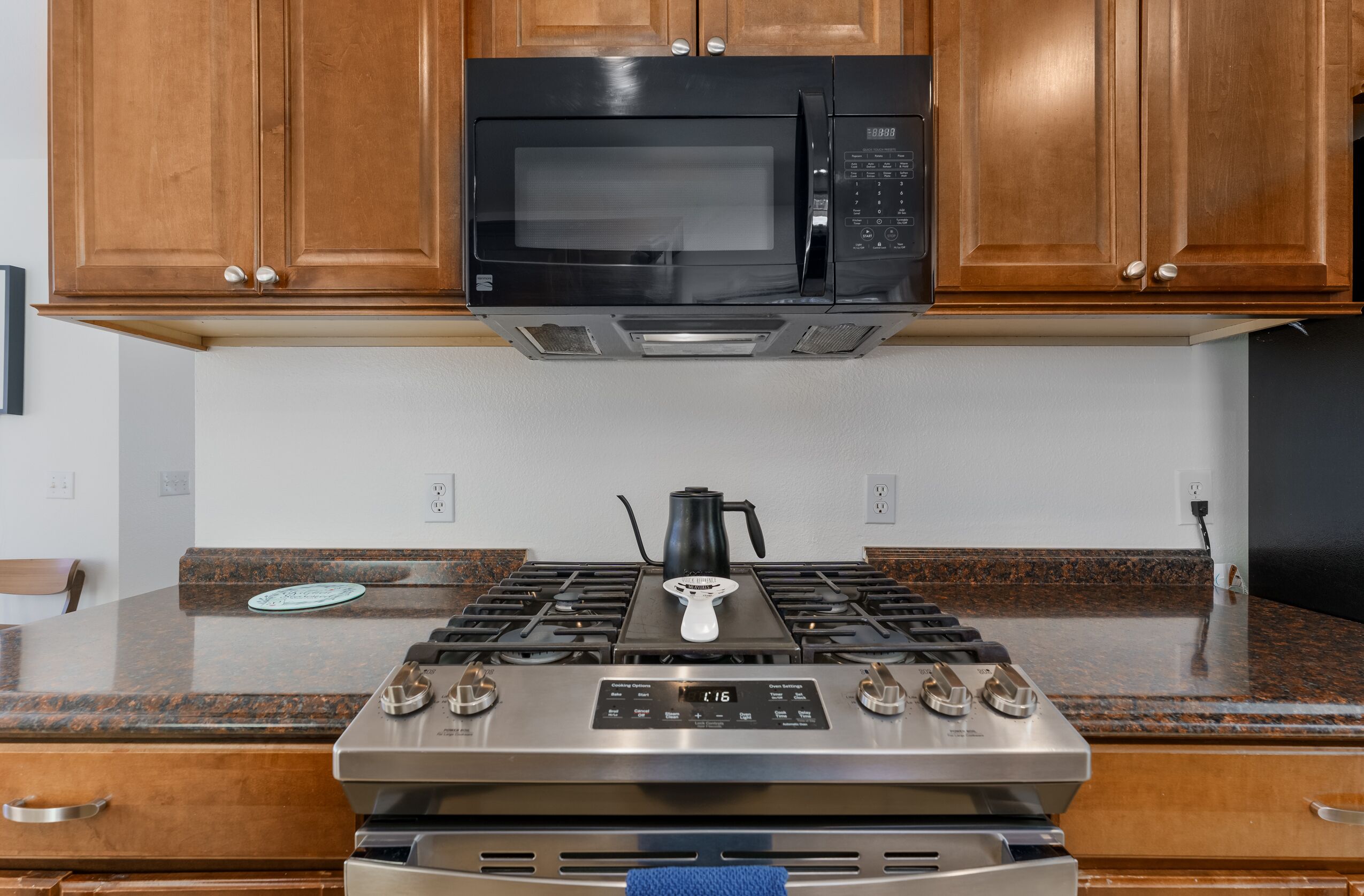A kitchen with wooden cabinets, a black microwave, a stainless steel stove, and a coffee maker.