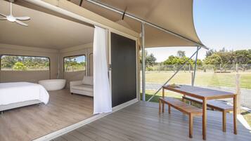 Una habitación amplia con cama, sofá, mesa de madera y un amplio ventanal corredera que da a un espacio exterior.