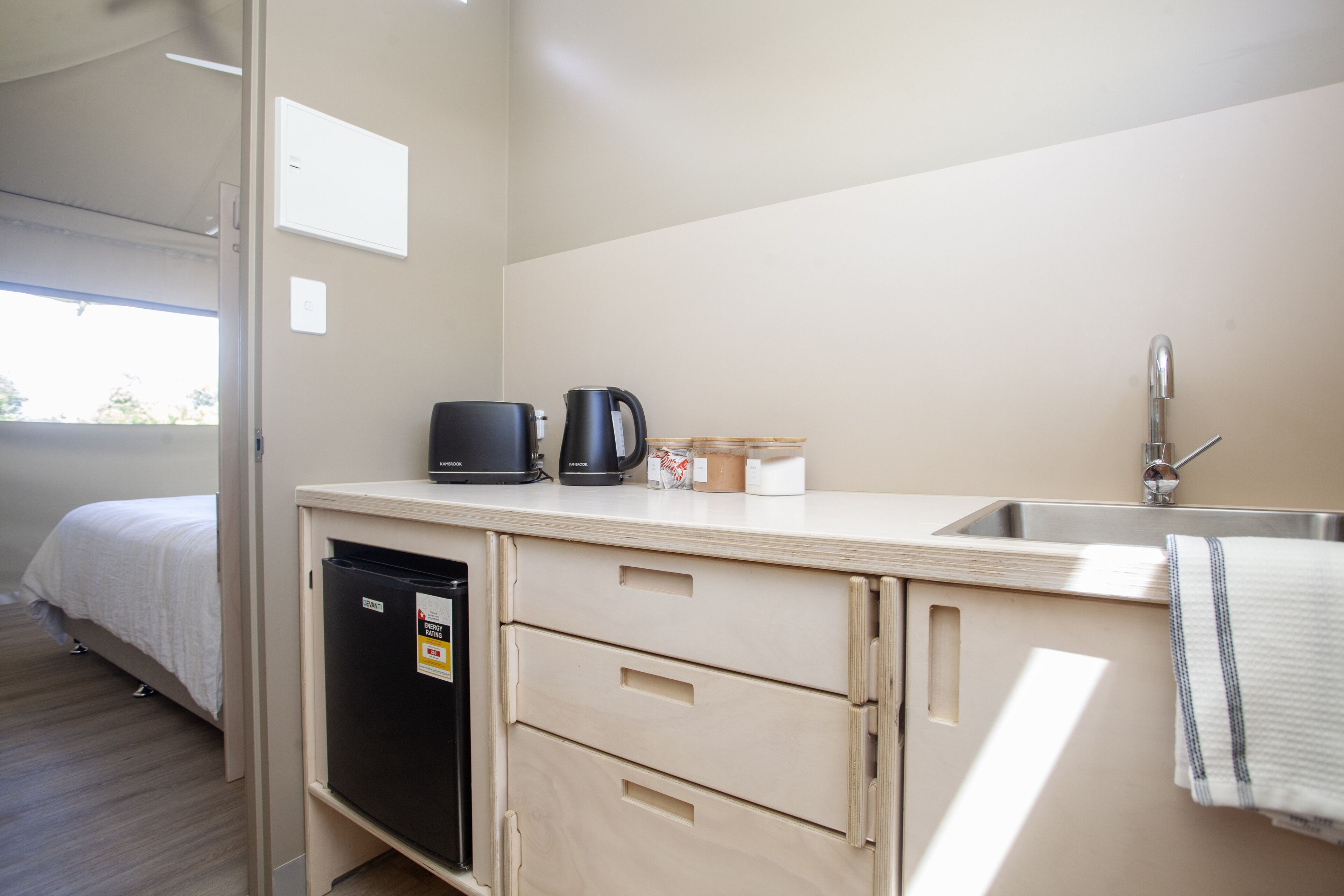 Una kitchenette compacta con un lavamanos, cafetera y un refrigerador pequeño.