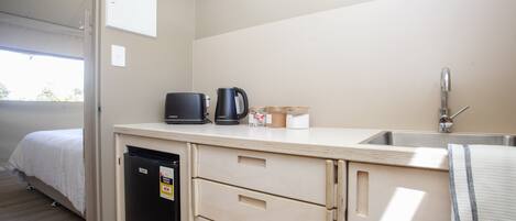 Una kitchenette compacta con un lavamanos, cafetera y un refrigerador pequeño.