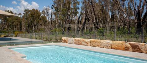 A rectangular pool with clear blue water, surrounded by a stone border and a fence.